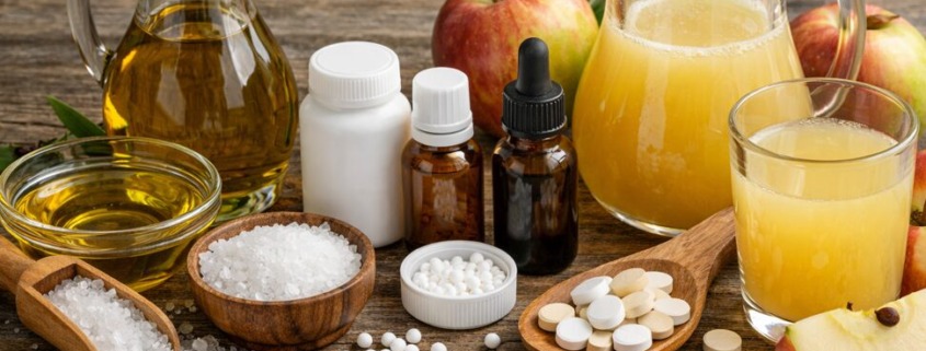 Olivenöl, Apfelsaft, Homöopathie und Schüßler-Salze als natürliche Mittel für eine Leberkur auf Holztisch arrangiert